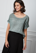 Woman wearing a green top and black pants against a white wall