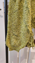A close-up of a chunky, fuzzy knit fabric in a mottled olive green and yellow colorway, draped over a black clothing rack.