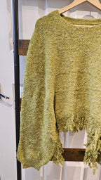 A textured, fuzzy knit sweater in a muted olive green-yellow color, hanging on a wooden hanger against a white paneled door.