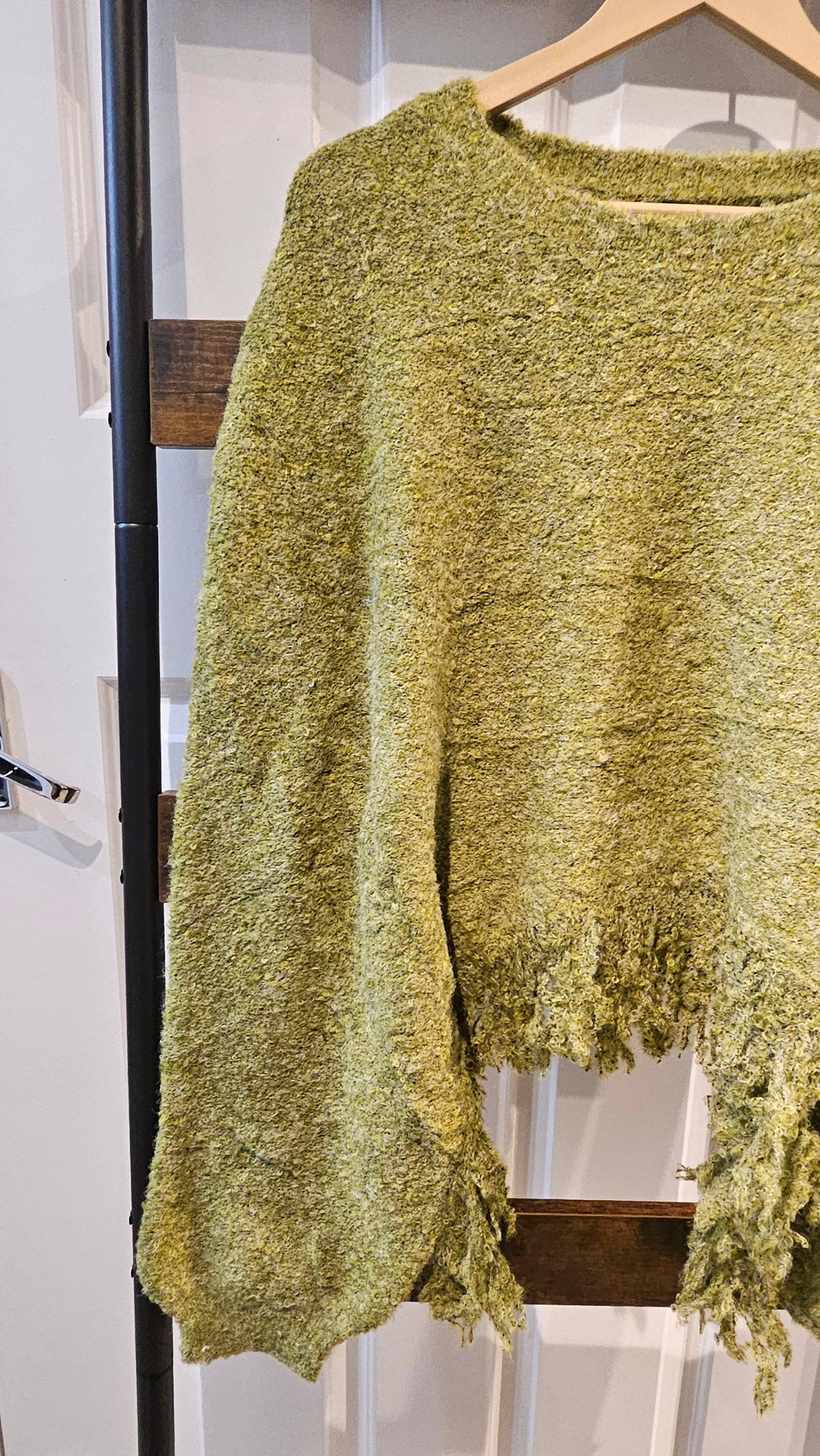 A textured, fuzzy knit sweater in a muted olive green-yellow color, hanging on a wooden hanger against a white paneled door.