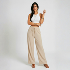 Woman wearing a white top and beige pants on a plain background