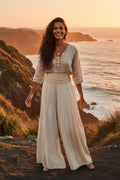 Woman in a flowing outfit standing on a coastal cliff at sunset