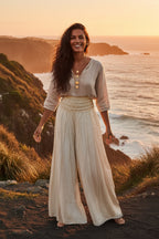 Woman in a flowing outfit standing on a coastal cliff at sunset