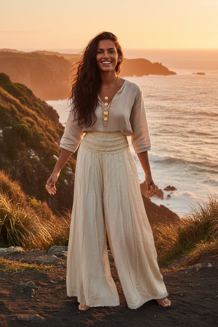 Woman in a flowing outfit standing on a coastal cliff at sunset