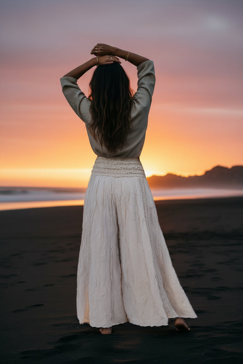 Woman standing on a beach at sunset with arms raised