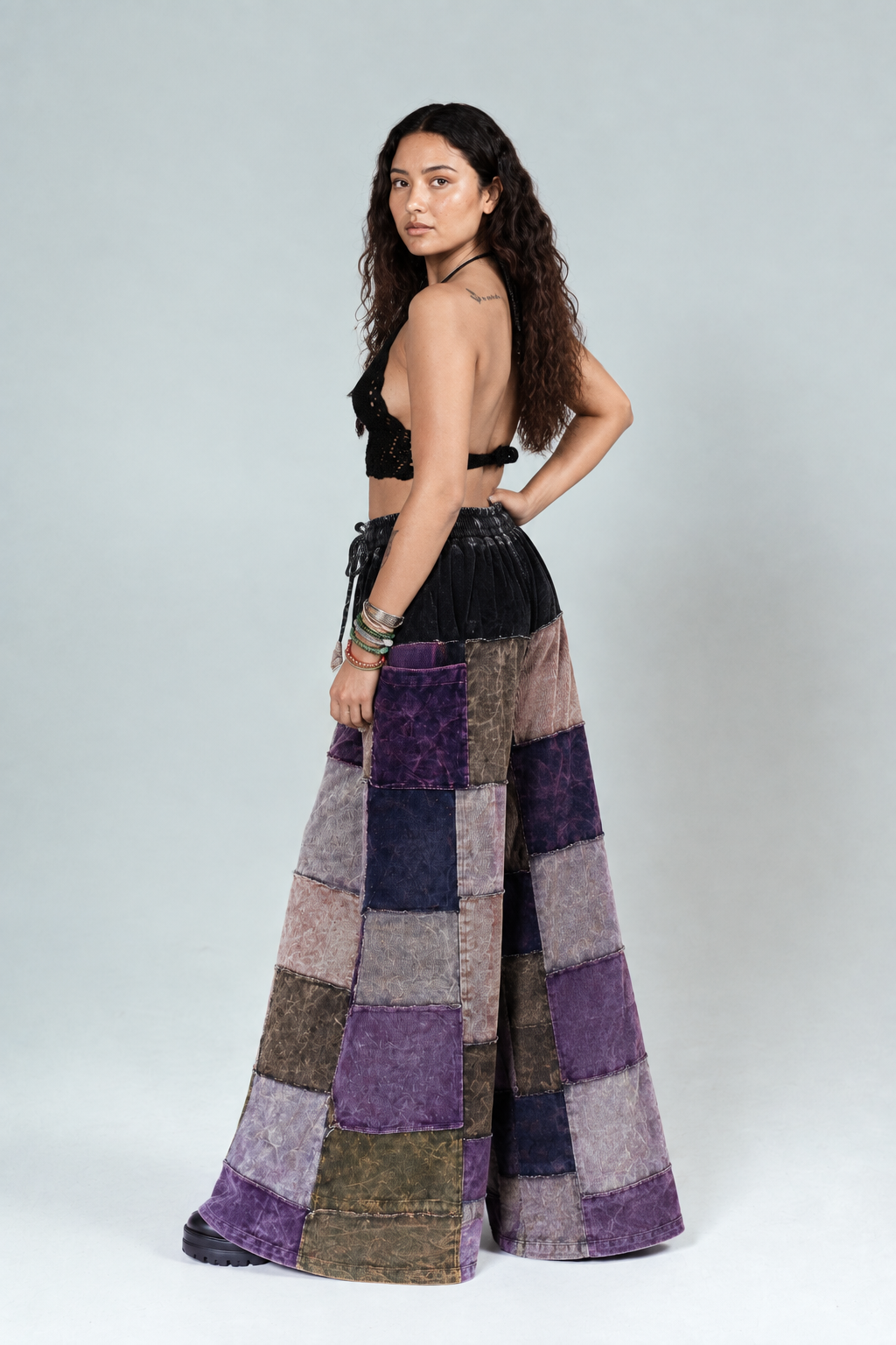Model standing in purple palazzo pants, hand on hip, turned to the opposite side