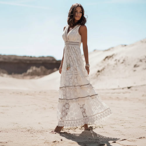 Woman in a white lace dress standing on sandy dunes with a clear blue sky.